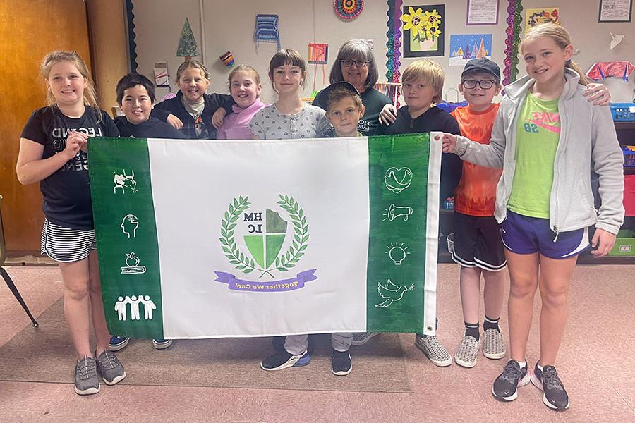 霍勒斯·曼恩的学生在萨拉·温特斯的五年级和六年级教室里, pictured with art teacher Lori Atkins, designed a flag to represent their school. (Submitted photo)